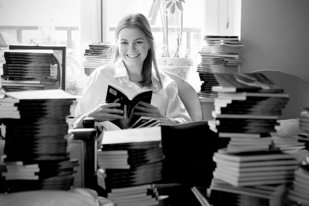 Emma Baizán sonriendo con un libro entre las manos, rodeada de pilas de libros